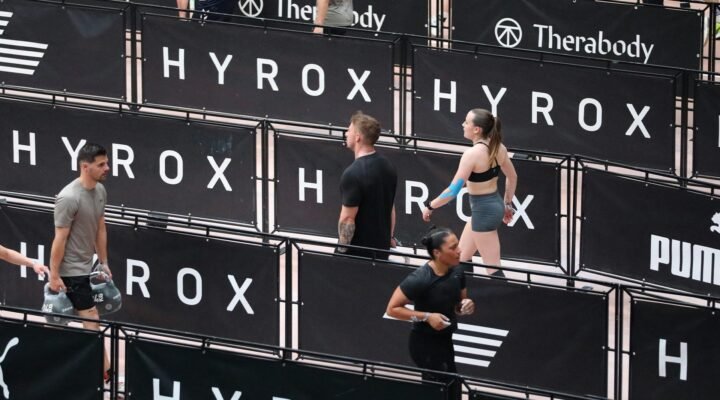 Athlètes Hyrox en récupération active sur parcours, phase de repos entre répétitions d'entraînement