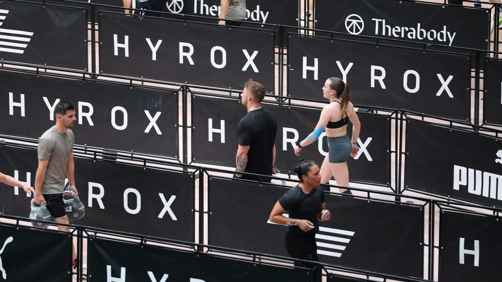 Athlètes Hyrox en récupération active sur parcours, phase de repos entre répétitions d'entraînement